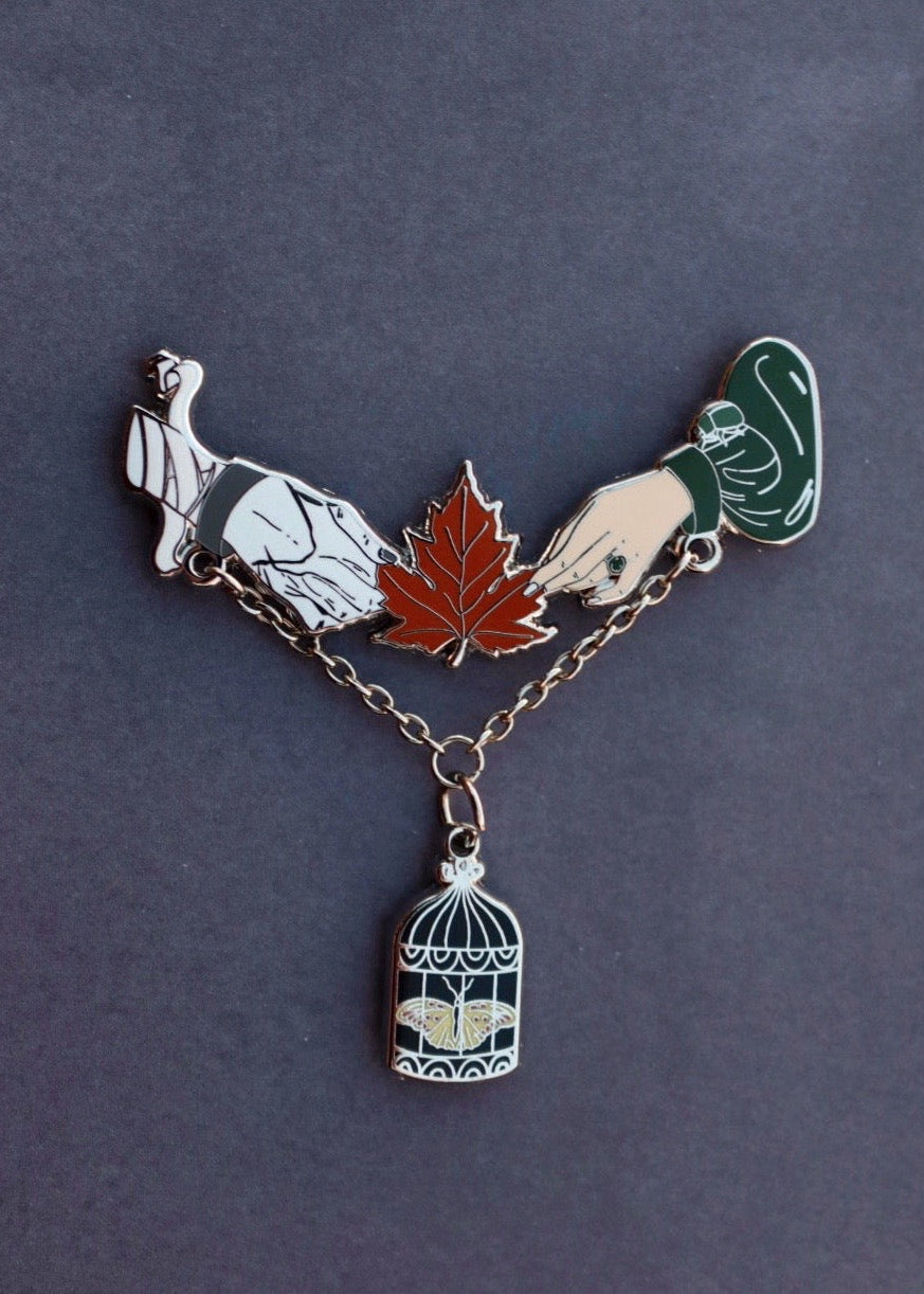Brooch with turtle, leaf, hand, and birdcage on a dark background